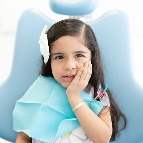 Young girl with hand to face wearing blue bib in dental office setting