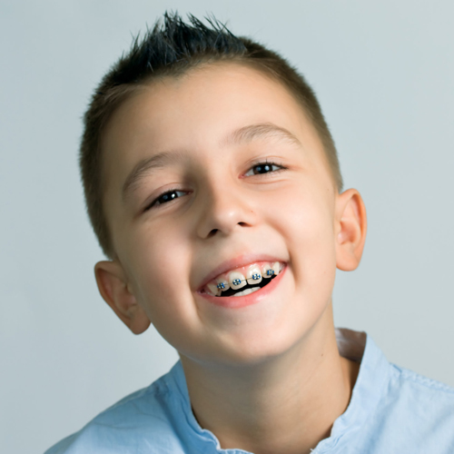 Young boy smiling at camera wearing light blue shirt against white background.