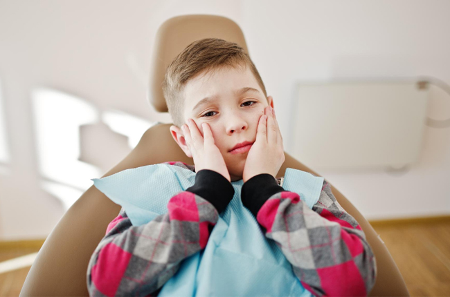 Young child with face paint sitting in dental chair, hands on cheeks, dental office setting.