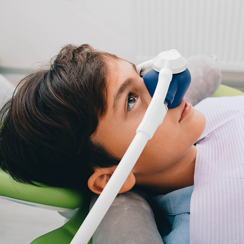 Child using blue and white inhaler while lying back in dental chair.