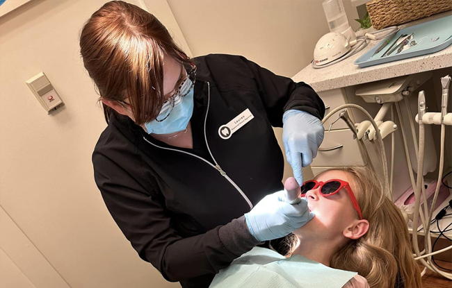 Pediatric dentist in black scrubs examining young patient's teeth in dental office.