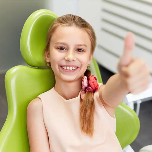 Happy young girl giving thumbs up in dental chair at pediatric dentistry office