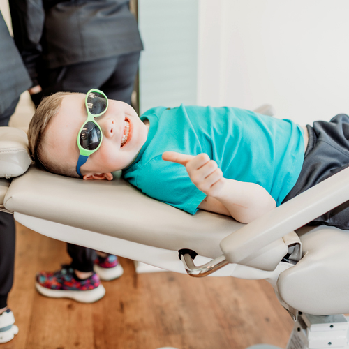 Young child wearing protective eyewear lying back in dental chair during examination.