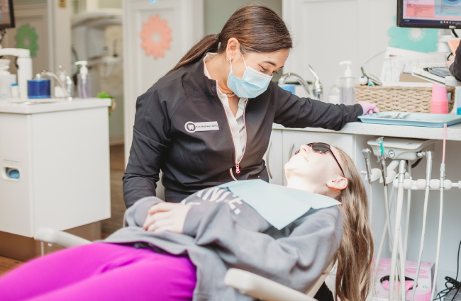 Pediatric dentist examining young patient's teeth in dental office treatment room.