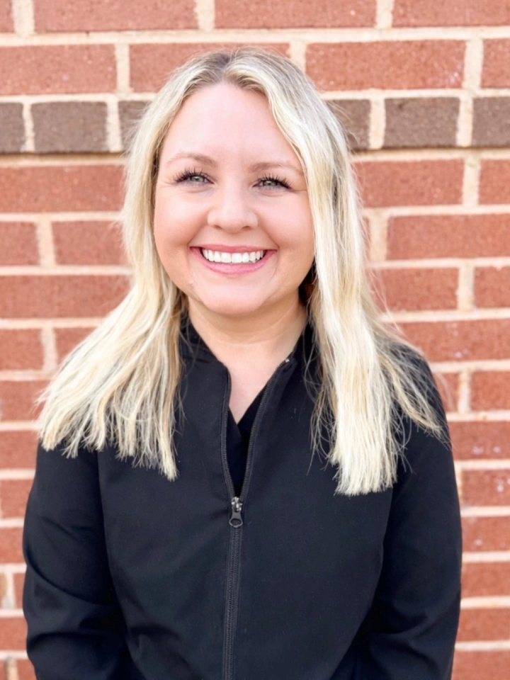 Professional woman with blonde hair smiling at camera against brick wall background
