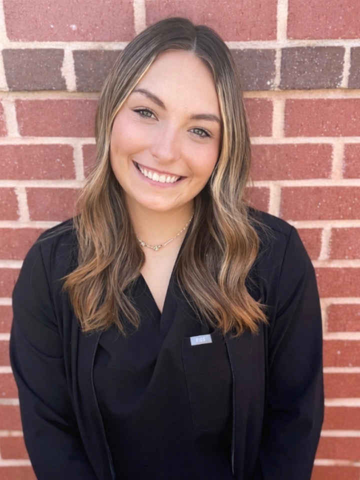 Professional woman smiling at camera wearing black blazer against red brick background