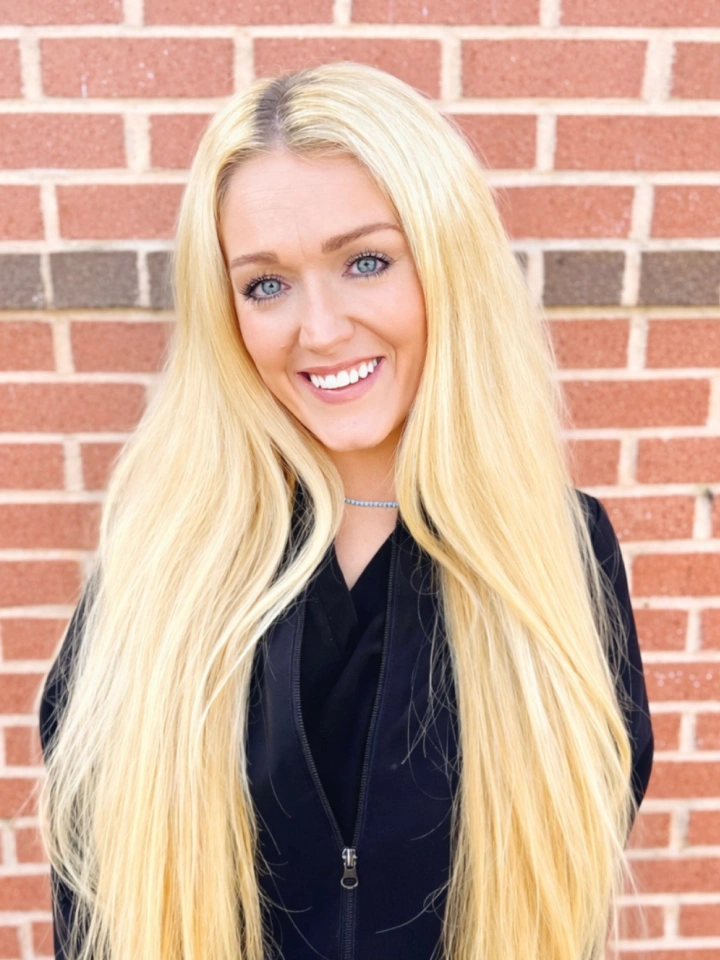 Blonde woman smiling at camera against brick wall background, professional headshot.