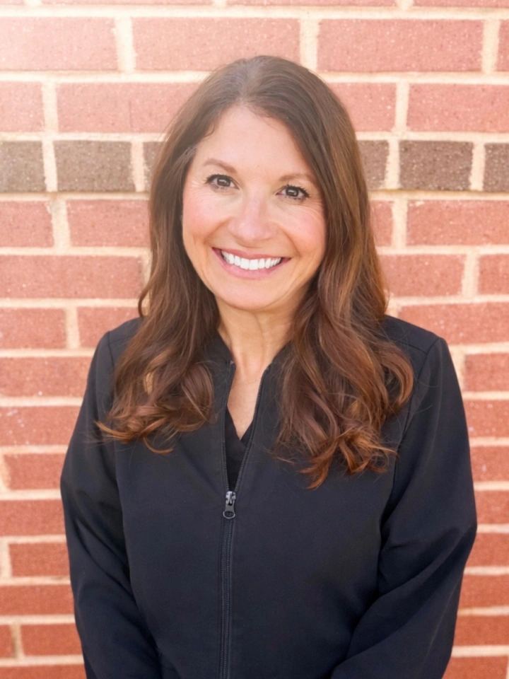 Professional headshot of smiling woman against red brick wall background.